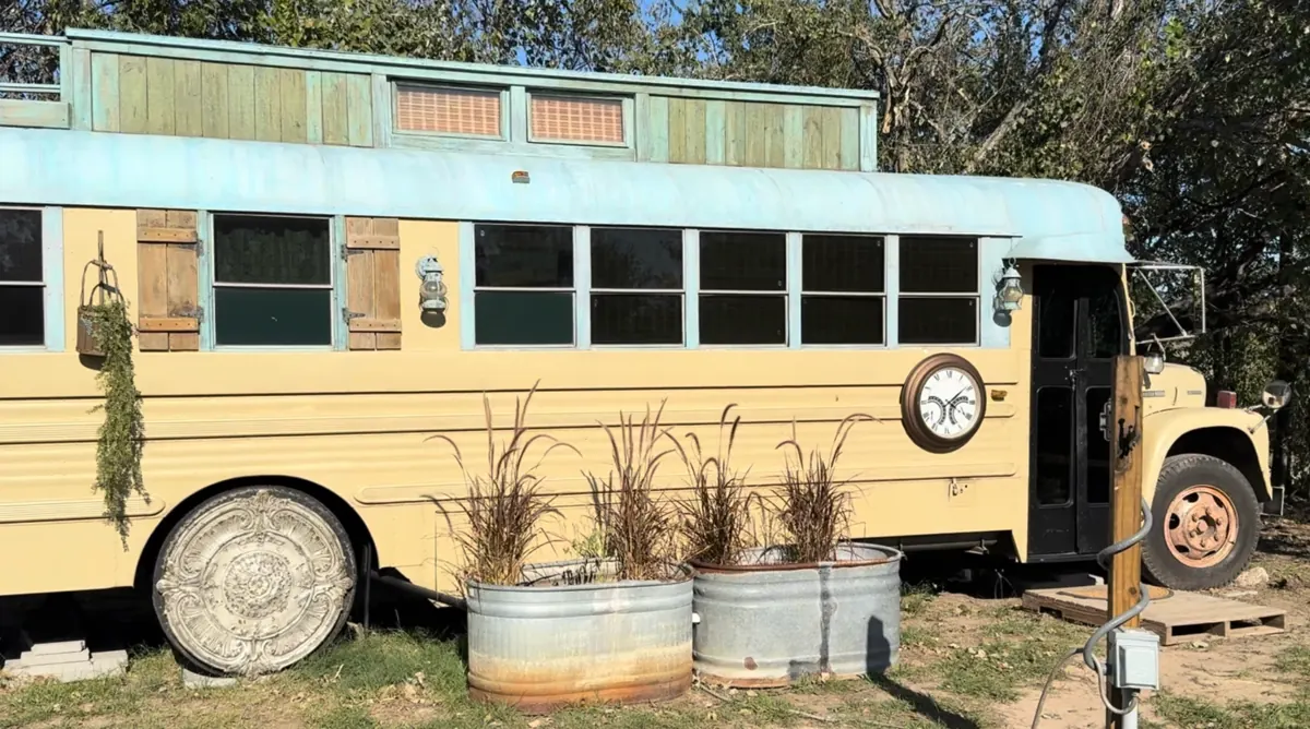 The Time Traveler: a buttercream vintage school bus with a sky-blue roof, wooden shutters and a big clock on its side