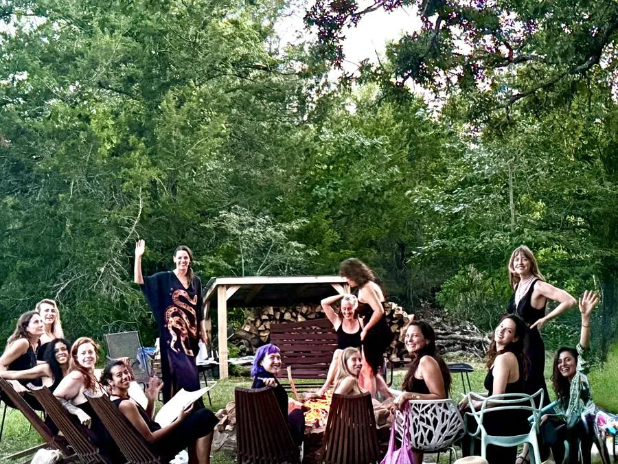 Women in black gathered around the fire circle by the woodshed