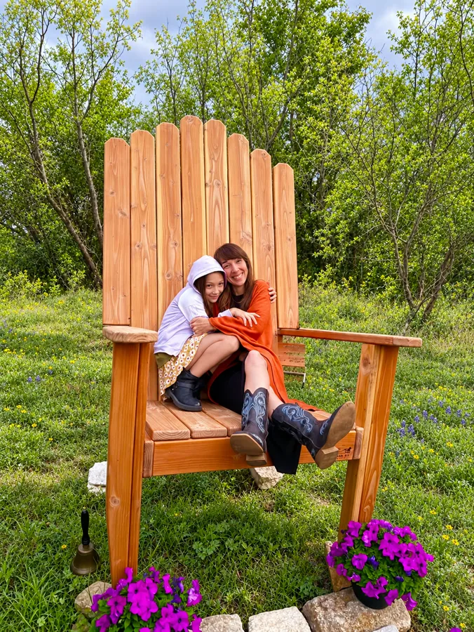 A woman and a girl cuddled in the giant wooden chair among wildflowers
