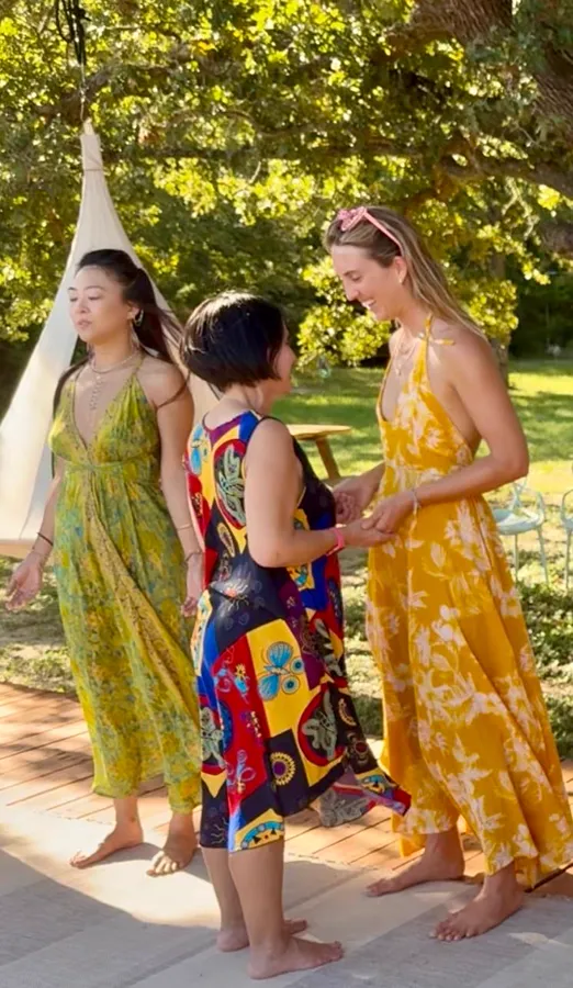 Three women in bright summer dresses by a tipi